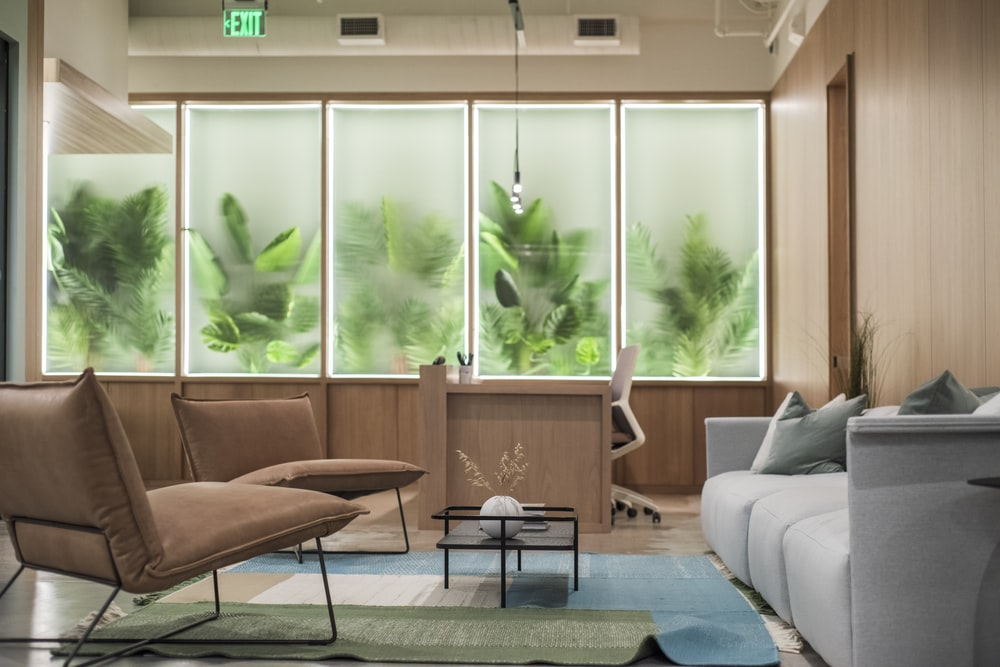 gray sofas and brown chairs in a room with plants.