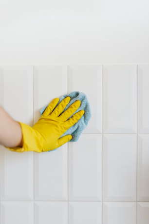 A hand in yellow rubber gloves cleaning a tile.