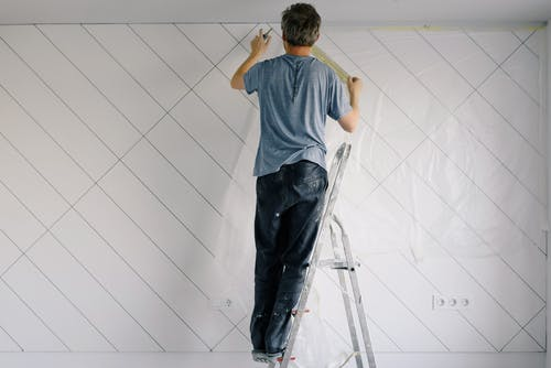 a man standing on a ladder making marks on the wall